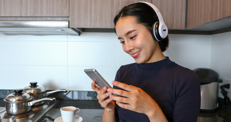 Asian women wearing headphone and listening to music in the kitchen at home