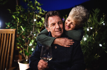 Senior couple with wine in the evening on terrace, hugging.