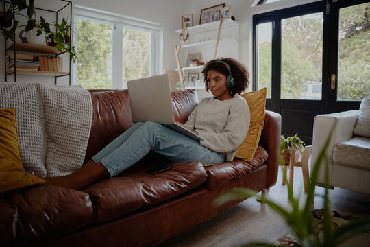 African Young Woman Relaxing On Couch While Watching Movie On Laptop With Wireless Bluetooth Headphones