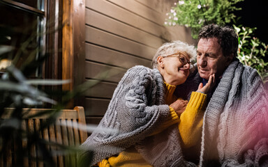 Portrait of senior couple sitting in the evening on terrace, hugging.