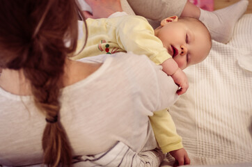 Little baby daughter lies on the lap of a young mother sitting on the couch