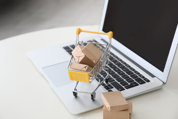Internet shopping. Laptop and small cart with boxes on white table indoors
