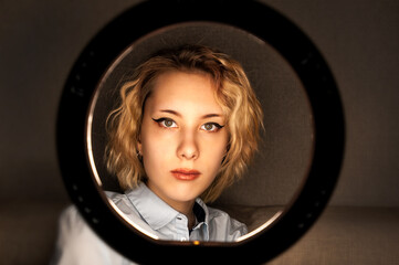 Portrait of a blogger girl working online with round lamp in the darkness . Indoors