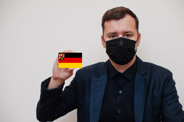 German man wear black formal and protect face mask, hold Rhineland-Palatinate flag card isolated on white background. Germany states coronavirus Covid concept.