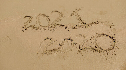 handwritten inscription 2020 and 2021 on sand of sea beach.