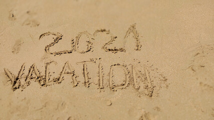 2021 Vacation handwritten inscription in sand of sea beach