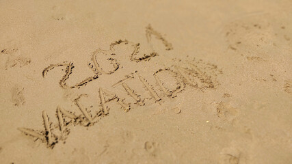 Text Vacation written in the sand of sea beach