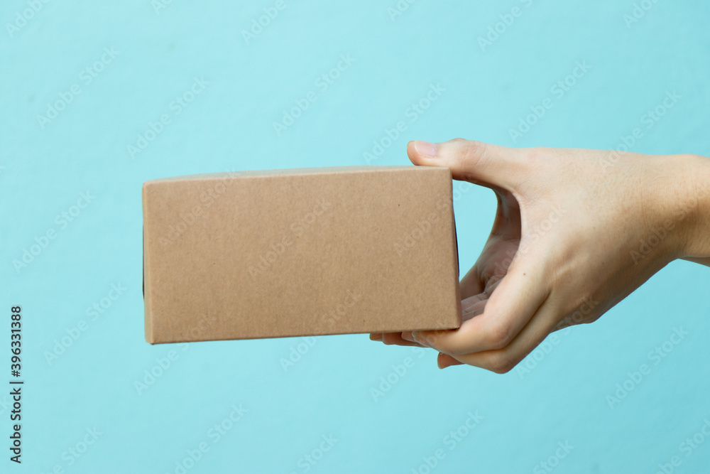 Wall mural Woman hand hold the brown corrugated box on blue  wall background with copy space