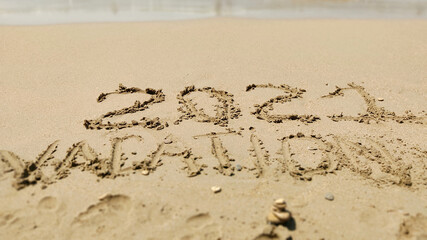 2021 Vacation handwritten inscription in sand of sea beach