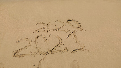 handwritten inscription 2020 and 2021 on sand of sea beach.