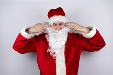 Man dressed as Santa Claus standing over isolated white background covering ears with fingers with annoyed expression for the noise of loud music. Deaf concept.