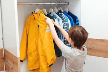Cute boy get dressed in the morning for school. Kid organizing clothes in wardrobe.