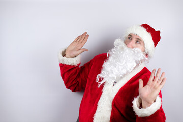 Man dressed as Santa Claus standing over isolated white background scared with her arms up like something falling from above