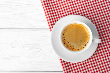 Cup of coffee on red checkered tablecloth top view