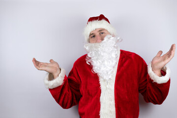 Fototapeta na wymiar Man dressed as Santa Claus standing over isolated white background clueless and confused expression with arms and hands raised