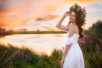 Fototapeta na wymiar Young woman wearing wreath made of beautiful flowers outdoors at sunset