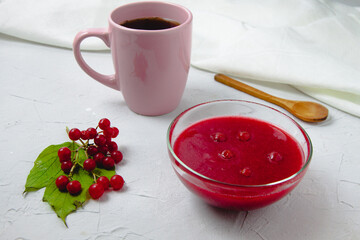 Autumn composition with viburnum jam, viburnum branches and leaves, white linen towel, pink cup, and wooden spoon. Concept of breakfast