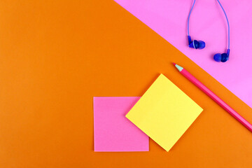 Bright orange and pink background with sheets of paper for writing, purple wired headphones and pencil