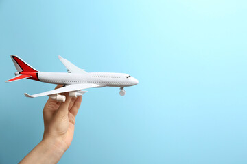 Woman holding toy airplane on light blue background, closeup. Space for text