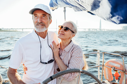 Mature woman in sunglasses embracing her husband and looking at him while he steering sailboat