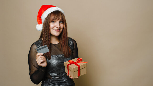 Image of a beautiful happy young woman posing isolated over beige wall background holding present gift box and credit card