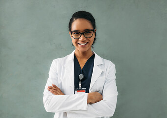 Portrait of smiling female doctor with crossed arms. Young medical specialist wearing eyeglasses and white jacket. - Powered by Adobe