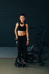 Fototapeta na wymiar Portrait of a sportswoman looking at camera standing in gym at air bike
