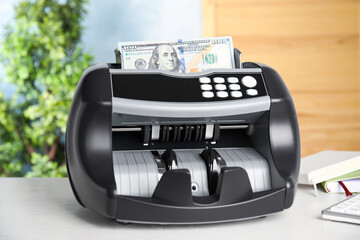 Modern electronic bill counter with money on table indoors