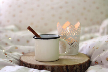 Enamel mug with warm drink and cinnamon stick and lit candle. Selective focus.