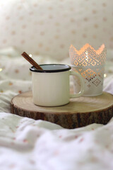 Enamel mug with warm drink and cinnamon stick and lit candle. Selective focus.