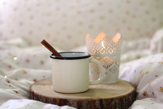 Enamel mug with warm drink and cinnamon stick and lit candle. Selective focus.