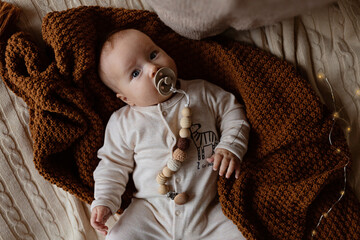 Cute caucasian baby girl lying on cozy bed with knitted plaid brown color. Happy childhood and...