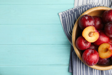 Delicious ripe plums in bowl on light blue wooden table, top view. Space for text