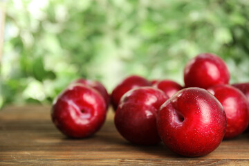 Delicious ripe plums on wooden table against blurred background, closeup. Space for text