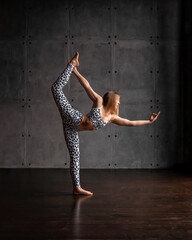 Girl doing yoga in a leopard suit. Natarajasana pose