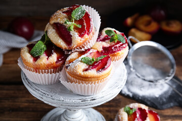 Delicious sweet cupcakes with plums on wooden stand, closeup