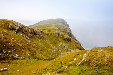 Rugged landscape at Malin Head, County Donegal, Ireland. Beach with cliffs, green rocky land with sheep on foggy cloudy day. Wild Atlantic Way region.