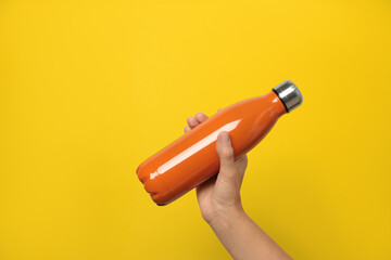 Woman holding modern orange thermos on yellow background, closeup