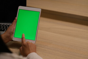 over the shoulder view of hand tapping green screen tablet in office