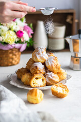 Woman sprinkles homemade profiteroles with sugar powder