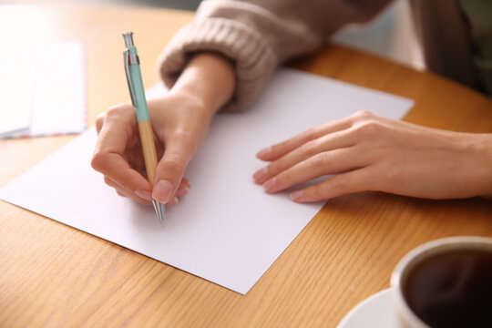 Woman writing letter at wooden table, closeup