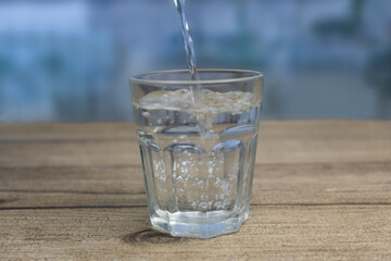 Fresh water pouring into glass on wooden table.Blurred background.