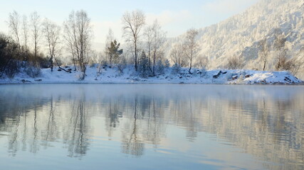 Panorama of river and snowy winter forest. Forest reflected in the lake.