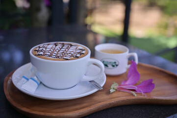 Coffee hot cappuccino cup on the wood tray on the dark table with hot tea on the white cup with purple color with natural light in the morning