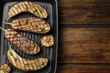 Delicious grilled eggplant halves in pan on wooden table, top view. Space for text