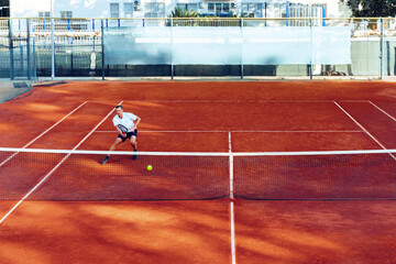 Man plays tennis on clay tennis field view from afar