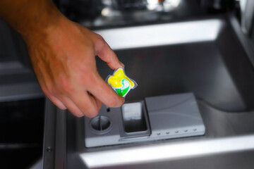 Close-up Of Person Hand Putting Tablet In Dishwasher Machine