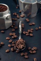 Metal spoon with coffee beans and coffee maker on dark textured background