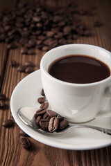 Cup of coffee with coffee beans on wooden textured table.