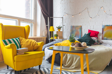Trendy fashion luxury interior design in Scandinavian style of studio apartment with bright yellow furniture and decorated with new year lights.